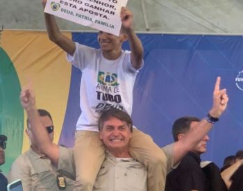 Na imagem o jovem subiu nos ombros do presidente com uma plaquinha. — Foto: Reprodução.