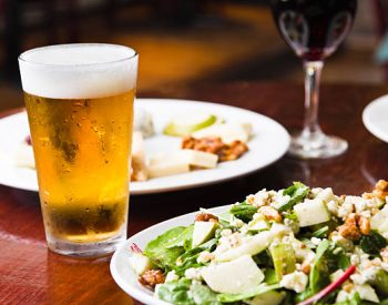 Icy cold beer with salad and appetizer dishes and red wine in a restaurant setting.  Beer glass has been frozen and shows condensation on the outside and a nice large head on the top.