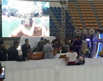 Namorada de Gabriel Diniz, Karoline Calheiros (centro, de camiseta branca junto ao caixão), agachada diante do caixão do cantor com familiares e fãs no velório, em ginásio de João Pessoa. ( Foto: André Resende/G1 )