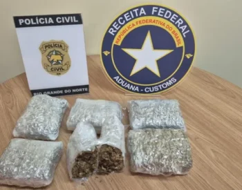Pacotes com material apreendido sobre mesa ao lado de identificações da Polícia Civil do Rio Grande do Norte e da Receita Federal